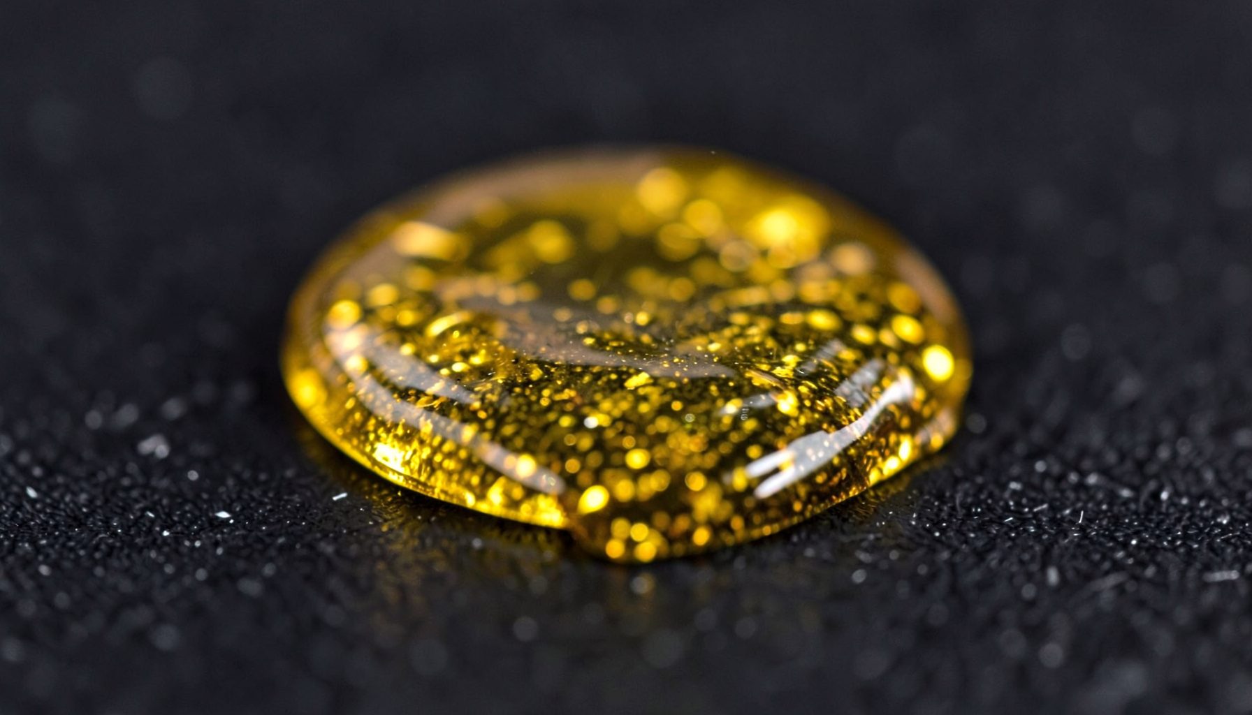 Translucent golden amber concentrate with a sparkling texture on a dark surface, warm gold and black tones