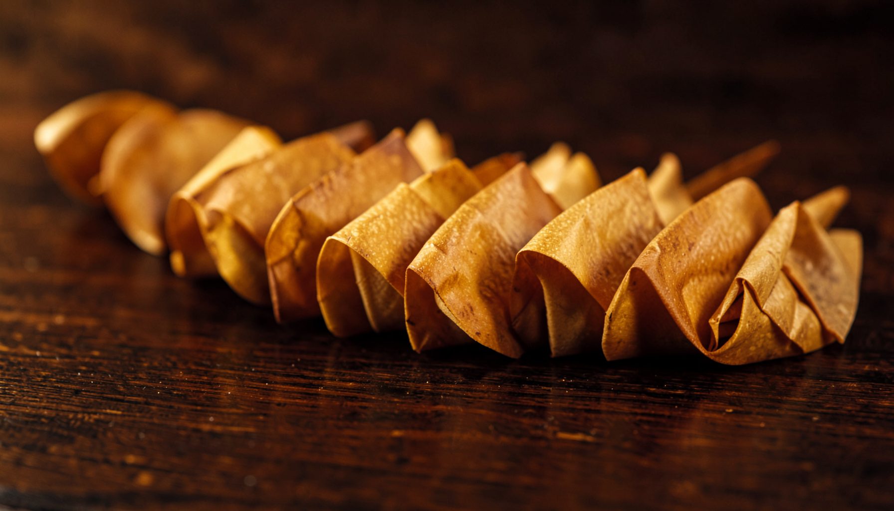 A row of tightly rolled pre-roll cones with golden tips resting on a dark wooden surface, warm amber and deep brown tones