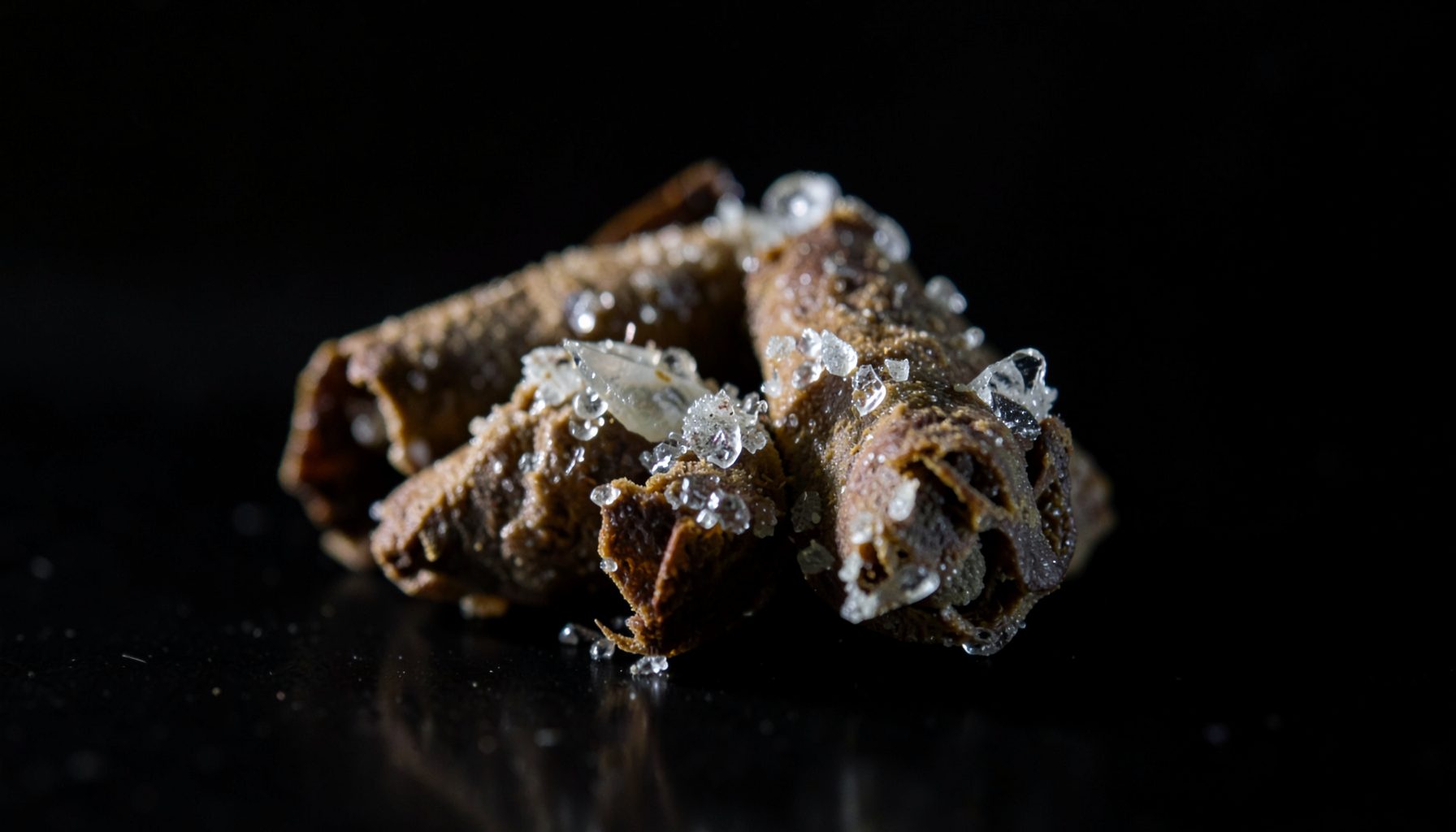 Infused pre-rolls with visible crystalline concentrate on the exterior, dark background with dramatic side lighting
