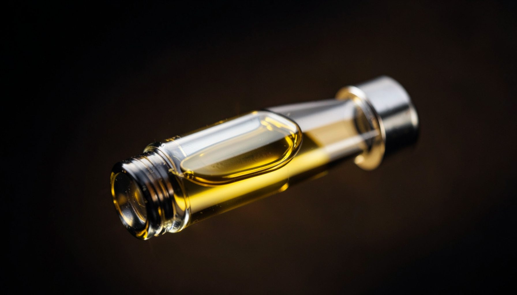 Close-up of a sleek glass vape cartridge with golden cannabis oil, set against a dark gradient background with subtle amber reflections