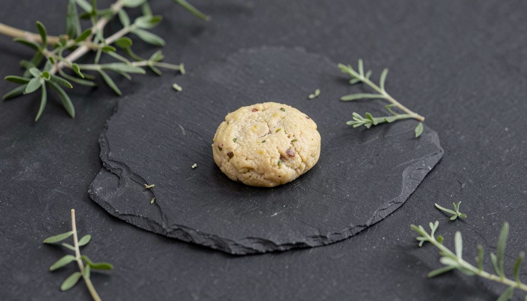 A single premium pre-roll resting on a dark slate surface with subtle green botanical accents