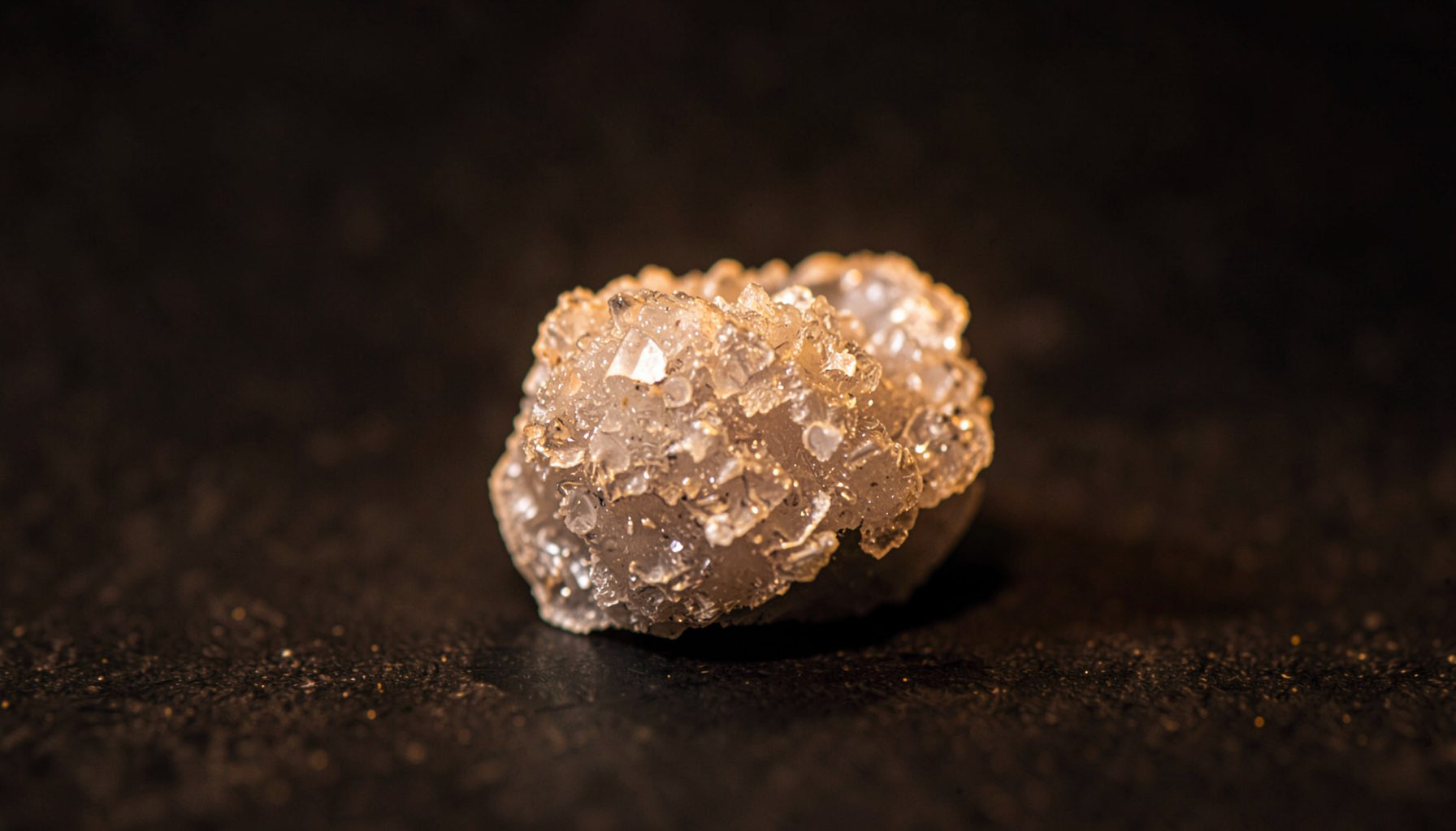 Translucent crystalline cluster with faceted formations on a dark speckled surface